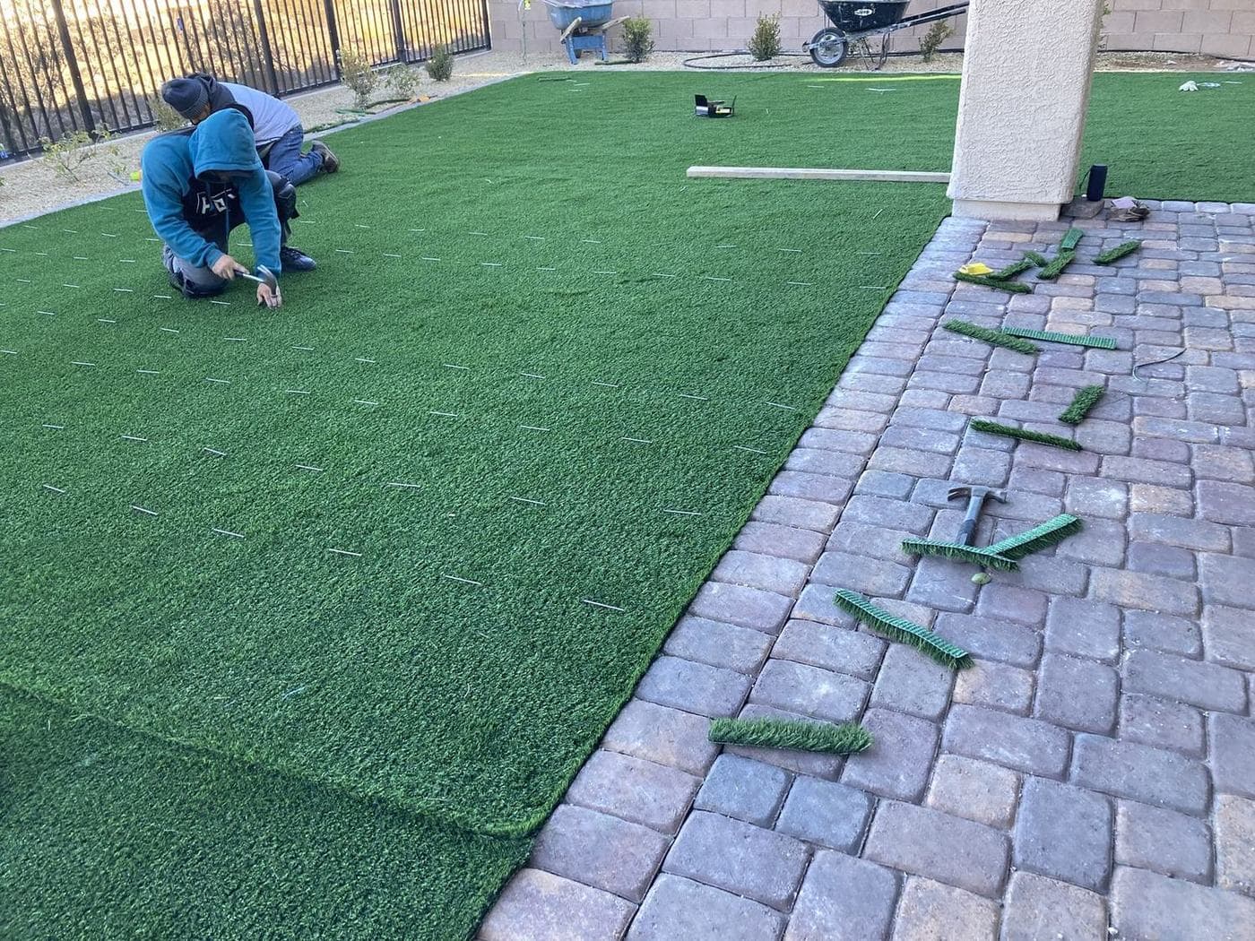 An A1 crew member installing artificial turf beside a new paver patio